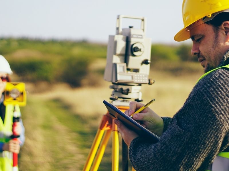 Land surveyor conducting a boundary survey and recording field measurements to verify property lines
